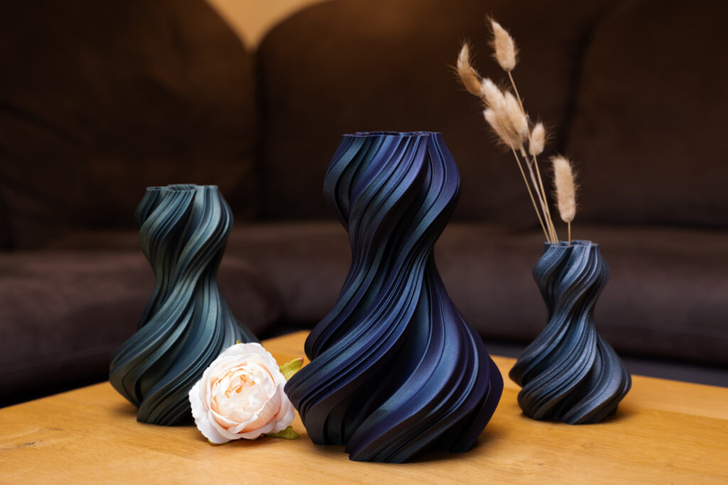 3D-gedruckte Vasen in Blau und Grün mit elegantem Spiralmuster, verziert mit einer Rose und getrockneten Gräsern.