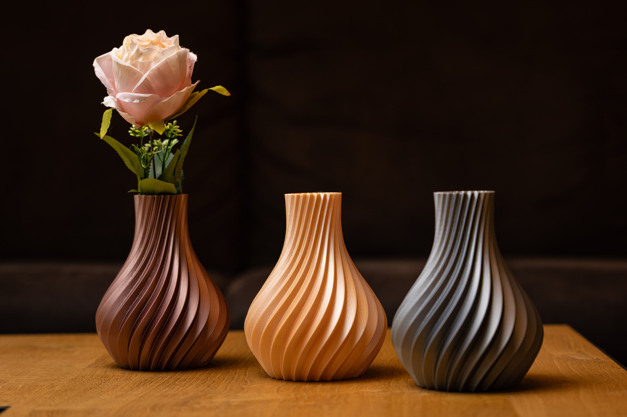 Drei elegante 3D-gedruckte Vasen in Erdtönen zeigen geschwungene Designs auf Holz, perfekt für moderne Dekorationen.