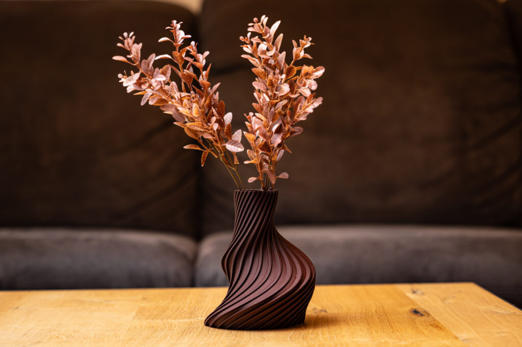 Moderne 3D-gedruckte Vase mit geschwungenem Design und warmen Farben, dekoriert mit Trockenblumen auf Holztisch.