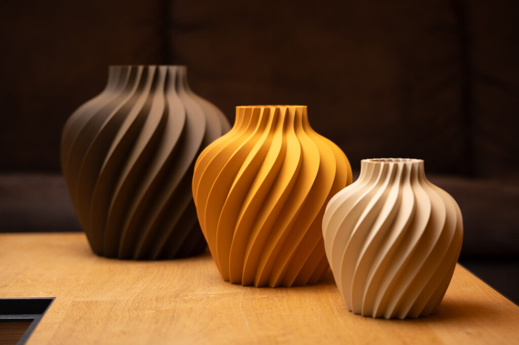 Drei elegant gedruckte 3D-Vasen in warmen Erdtönen, mit spiralförmigen Mustern auf einem Holztisch arrangiert.