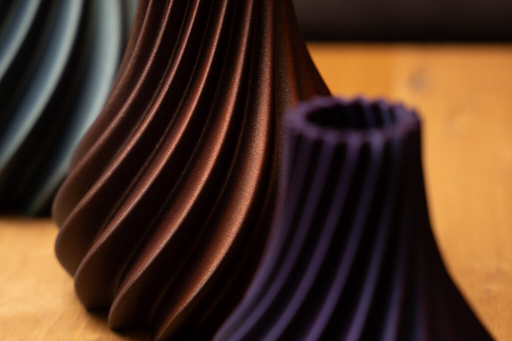 3D-gedruckte Vasen mit spiralförmigem Design, braun und dunkelviolett, elegante moderne Deko auf Holztisch.