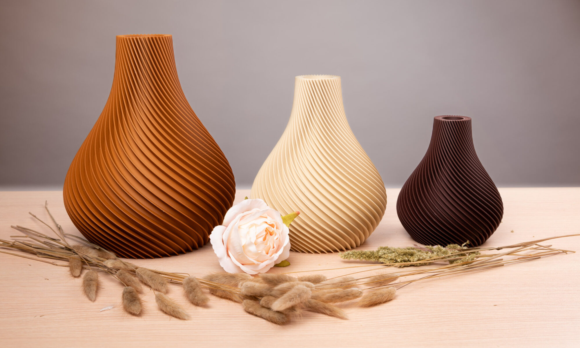 Drei 3D-gedruckte Vasen in Braun-, Beige- und Dunkelbrauntönen mit spiralförmigem Muster, dekoriert mit Trockenblumen.
