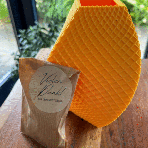 Gelbe, 3D-gedruckte Vase mit strukturierter Oberfläche neben einem Dankeschön-Paket auf einem Holztisch.