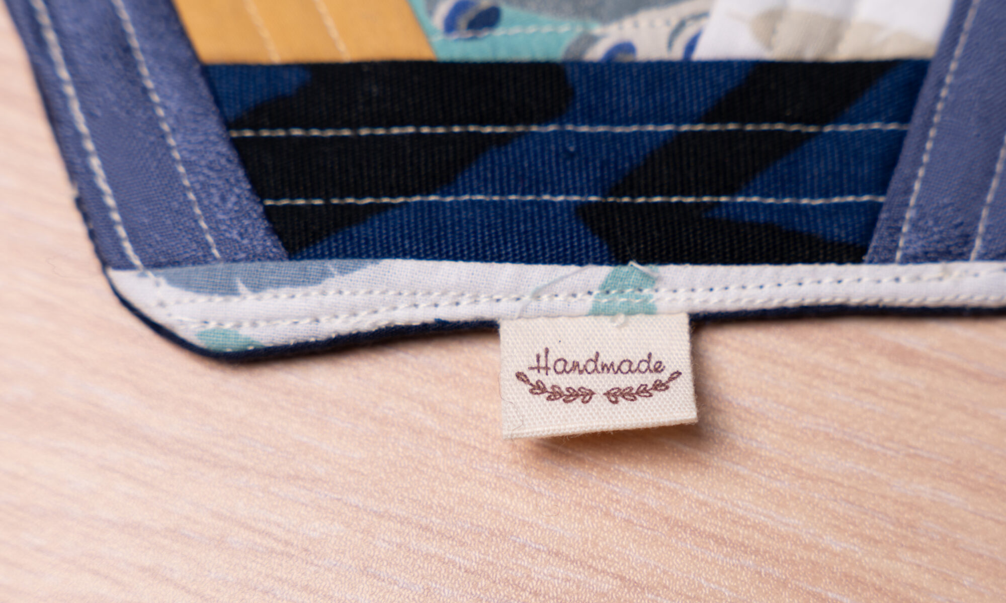 Handgefertigtes Patchwork mit blauen und gelben Mustern und einem Handmade-Etikett auf Holzoberfläche, stilvoll designt.