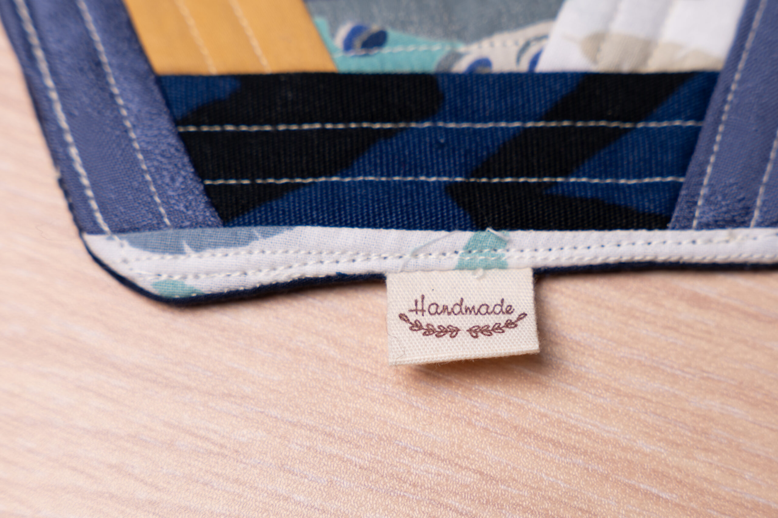 Handgefertigtes Patchwork mit blauen und gelben Mustern und einem Handmade-Etikett auf Holzoberfläche, stilvoll designt.