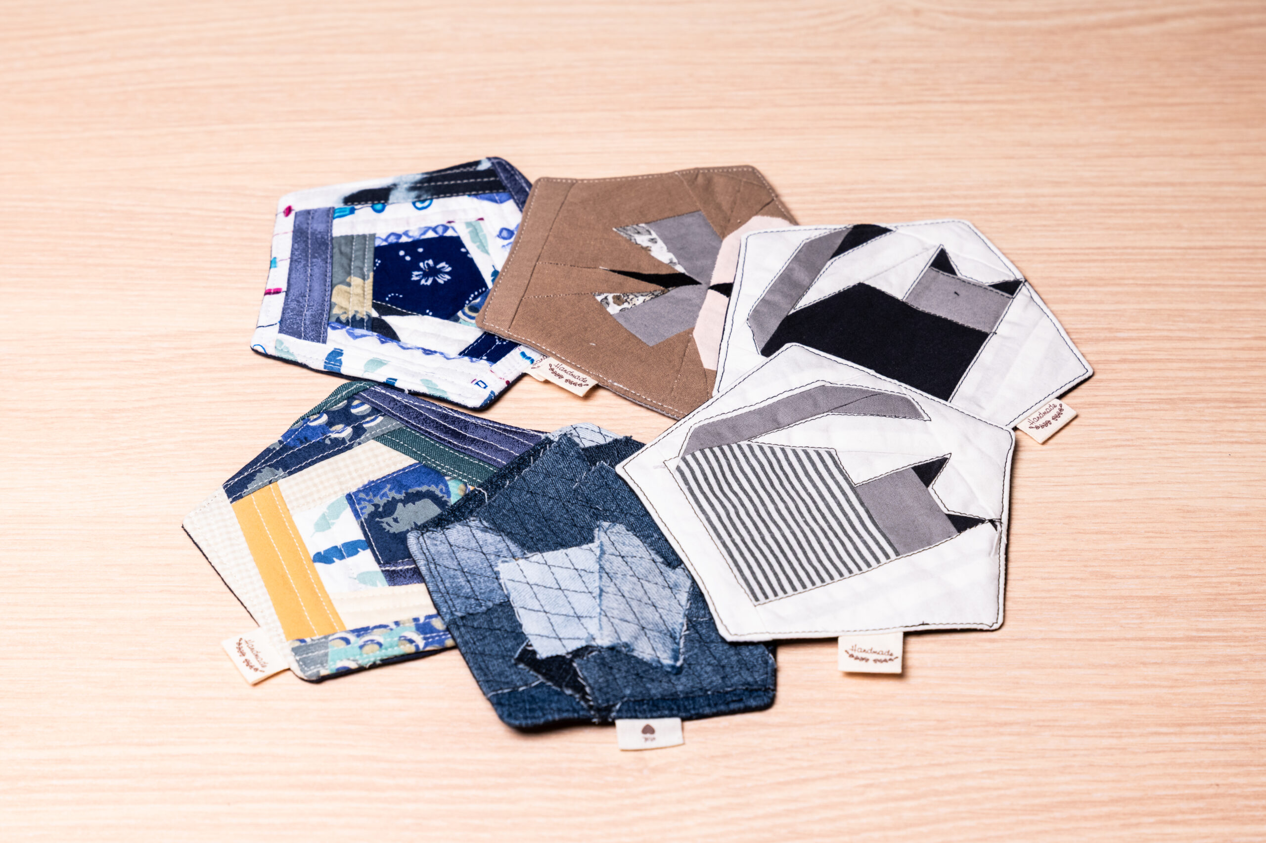 Handgenähte Untersetzer aus bunten Stoffresten mit geometrischen Mustern auf einem Holzuntergrund für stilvolle Dekoration.