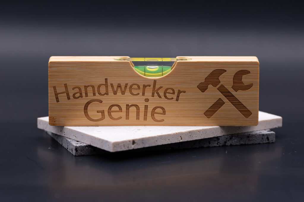 Holzwasserwaage mit Gravur Handwerker Genie, auf Marmorplatte platziert. Stilvolles Design, perfekt für kreative Heimwerker.