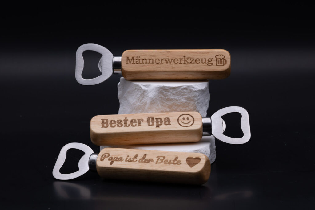 Hochwertige, gravierte Flaschenöffner mit personalisierten Botschaften auf Holzgriff vor schwarzem Hintergrund.