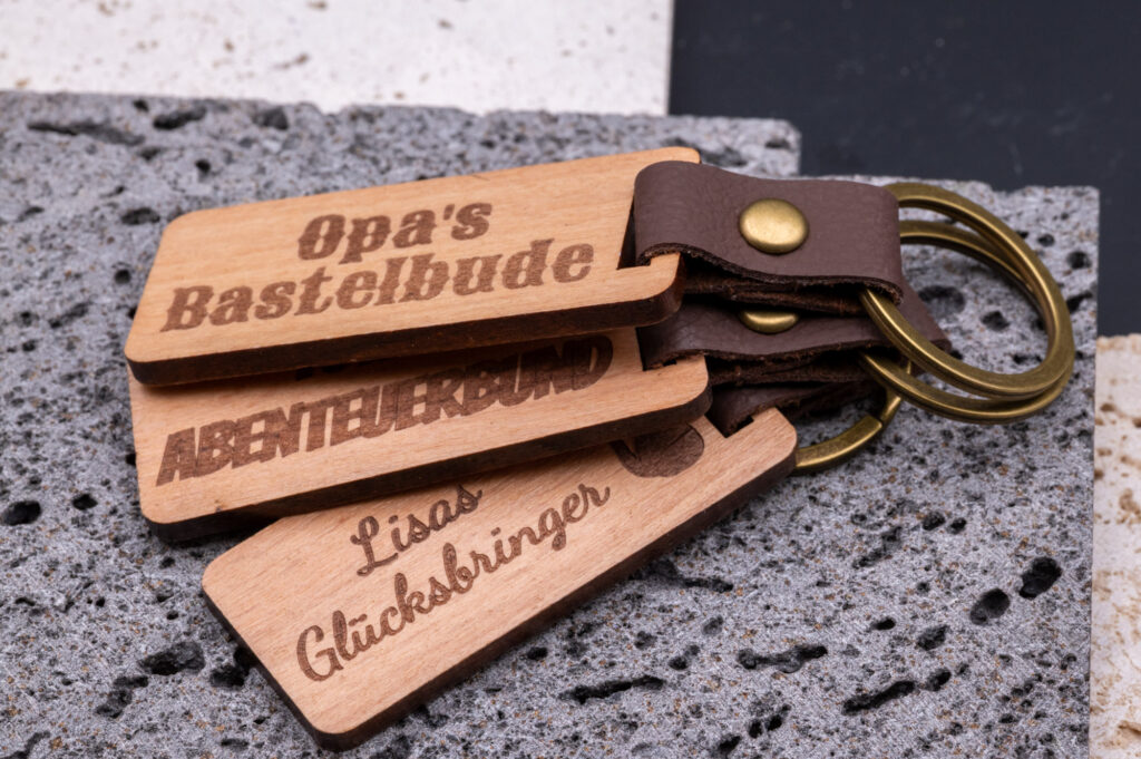 Holzschlüsselanhänger mit Gravur: Opa's Bastelbude, Abenteuerbund, Lisas Glücksbringer, stilvoll auf Stein.