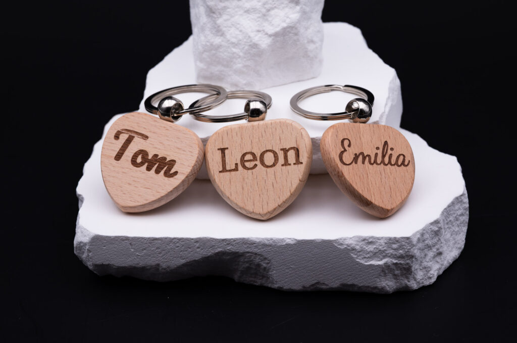 Herzförmige Schlüsselanhänger aus Holz mit Gravuren: Tom, Leon, Emilia. Natürlicher Look, ideal als persönliches Geschenk.