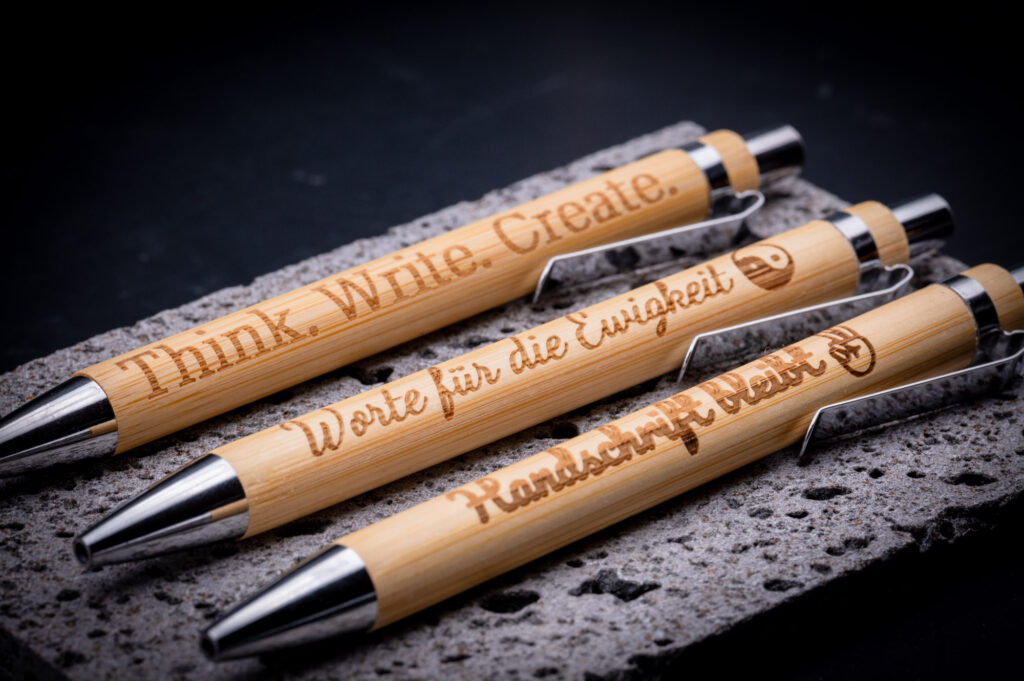 Drei elegante Kugelschreiber aus Bambus mit inspirierenden Gravuren, präsentiert auf Betonoberfläche für mydesignstyle.com.