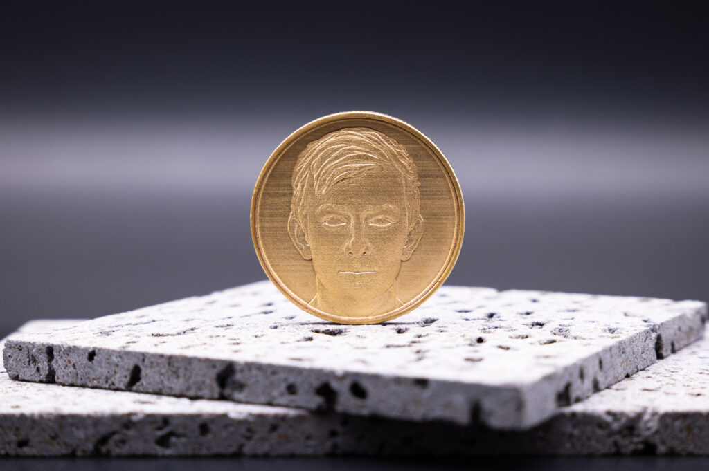 Goldene Medaille mit stilisiertem Gesicht auf grauer, strukturierter Steinplatte platziert, edel und detailreich gestaltet.