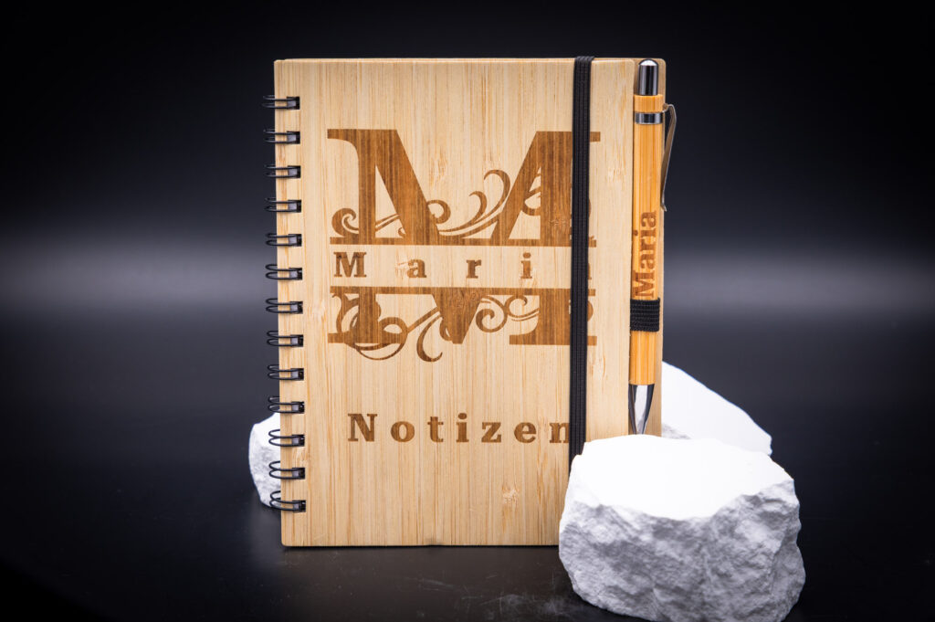 Elegantes Notizbuch aus Bambus mit personalisiertem Stift in edlem Design, ideal für stilvolle Notizen, präsentiert auf hellem Stein.