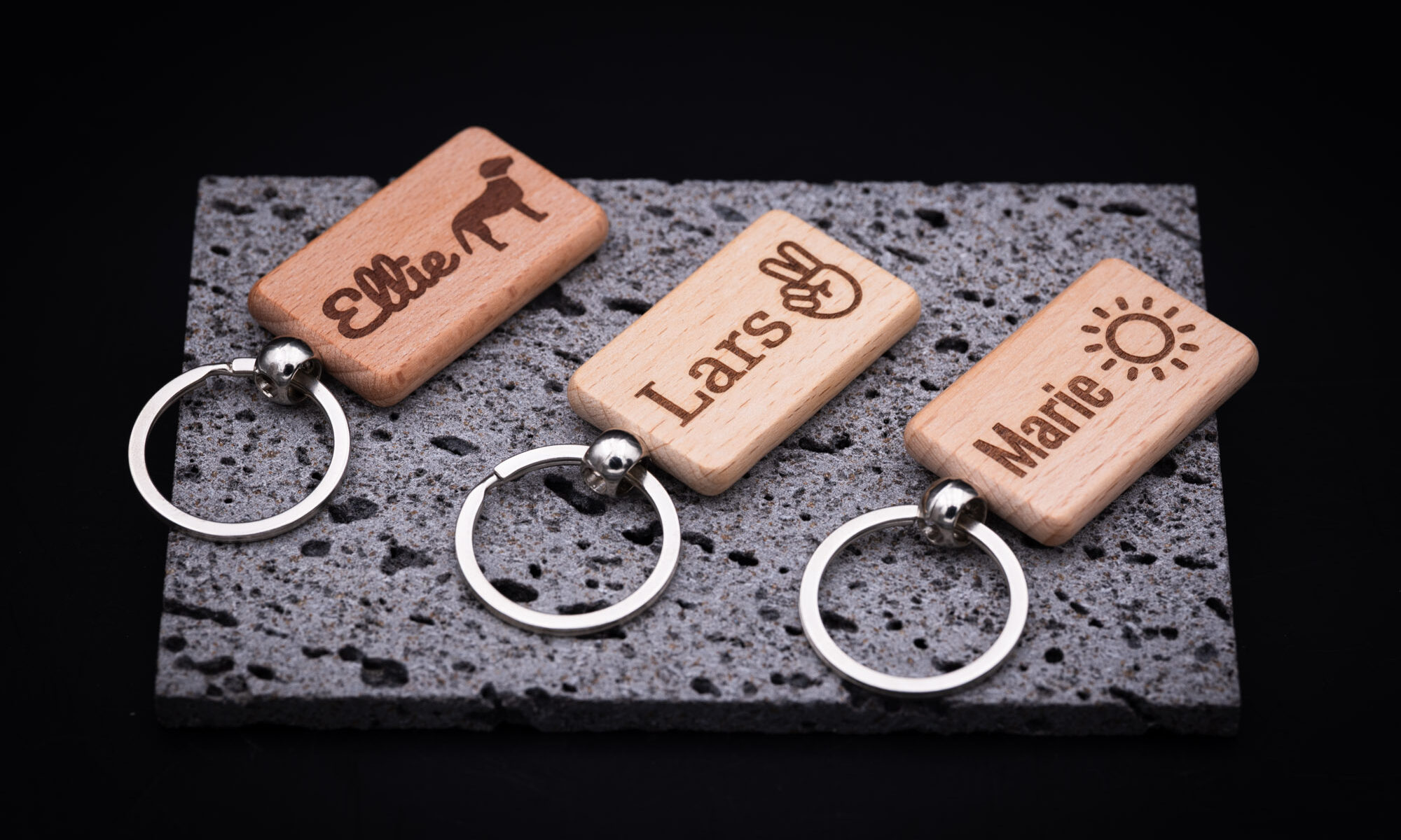 Personalisierte Holzschlüsselanhänger mit Gravur auf edler grauer Steinplatte, stilvoll und einzigartig präsentiert.