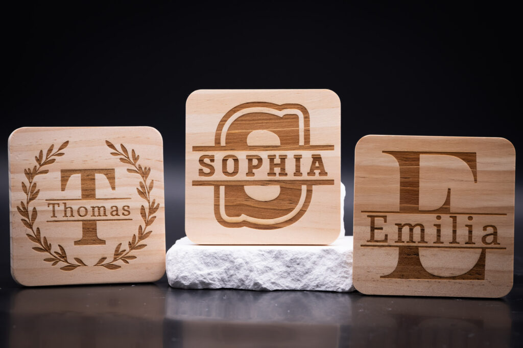 Personalisierte Holzuntersetzer aus hellem Holz mit den Namen Thomas, Sophia und Emilia, stilvoll graviert.