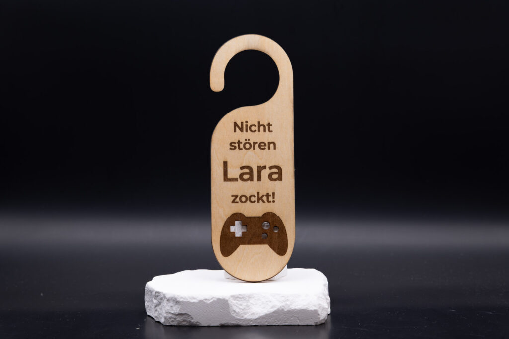 Holz-Türschild mit Nicht stören Lara zockt!-Gravur, stilvoll auf weißem Podest präsentiert, modernes Design.