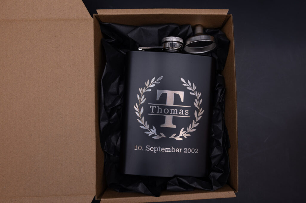 Personalisierte, schwarze Edelstahlflasche mit Gravur Thomas und Datum, edel verpackt in brauner Geschenkbox.