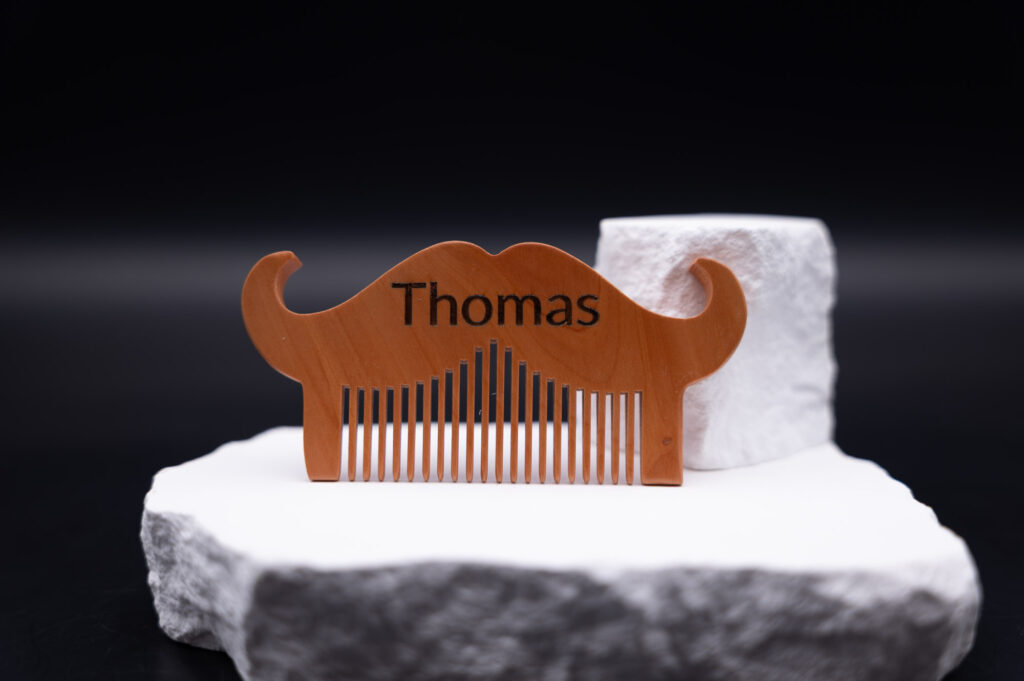 Holzkamm in Schnurrbartform mit Gravur Thomas, kunstvoll inszeniert auf weißem Stein für einen eleganten Look.