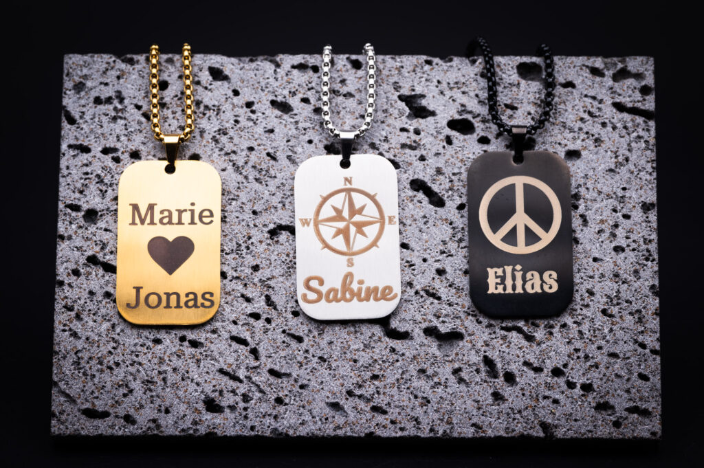 Drei stilvolle Namensanhänger aus 3D-Druck: Gold mit Herzmotiv, Silber mit Kompass, Schwarz mit Peace-Zeichen. Elegant designt.
