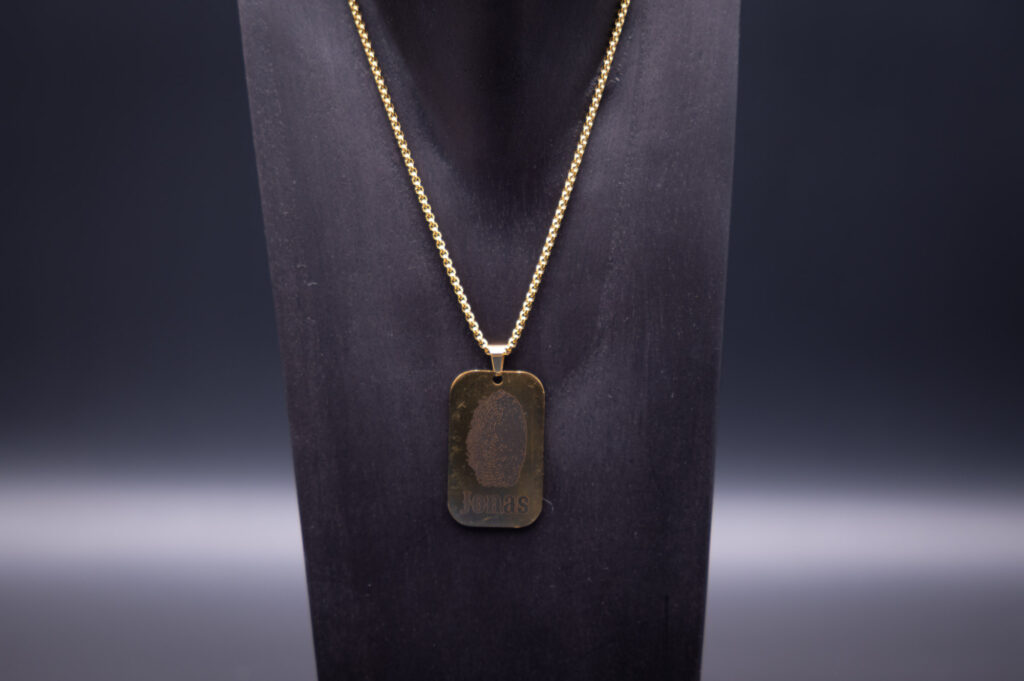 Elegantes goldenes Namensschild an Kette, stilvoll präsentiert auf dunklem Hintergrund von mydesignstyle.com.