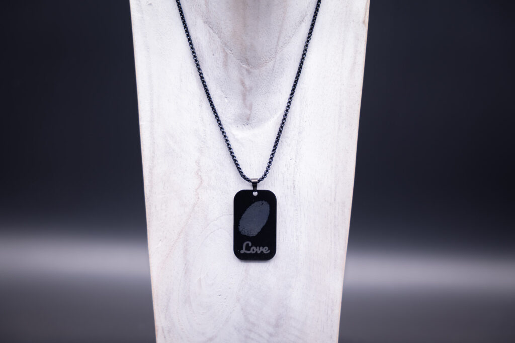 Schwarze Halskette mit Anhänger, Fingerabdruck und Love-Gravur auf elegantem weißem Hintergrund präsentiert.