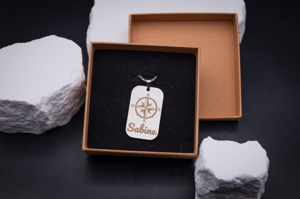 Personalisiertes Kompass-Schmuckstück in edler Geschenkbox auf schwarzem Hintergrund, mit dem Namen Sabine graviert.