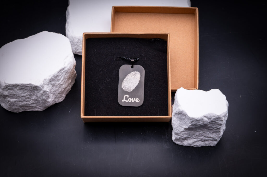 Schmuckanhänger in Geschenkschachtel auf schwarzem Hintergrund, dekoriert mit weißen 3D-gedruckten Steinen, edel und elegant.