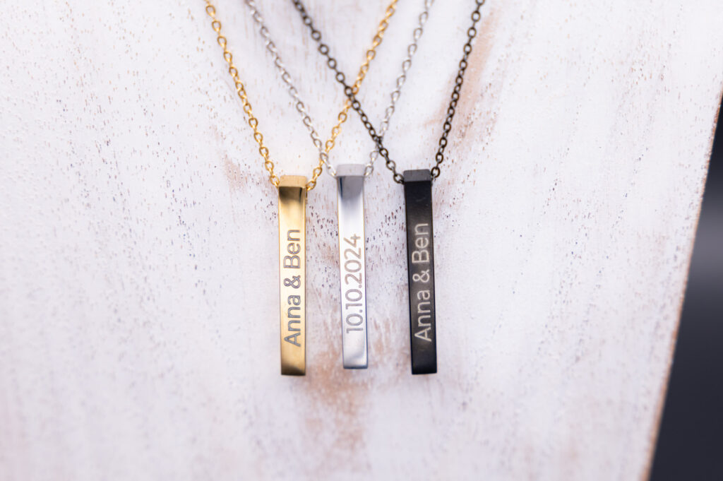 Drei elegante Namensketten in Gold, Silber und Schwarz mit personalisiertem Gravurtext, stilvoll präsentiert auf hellem Hintergrund.