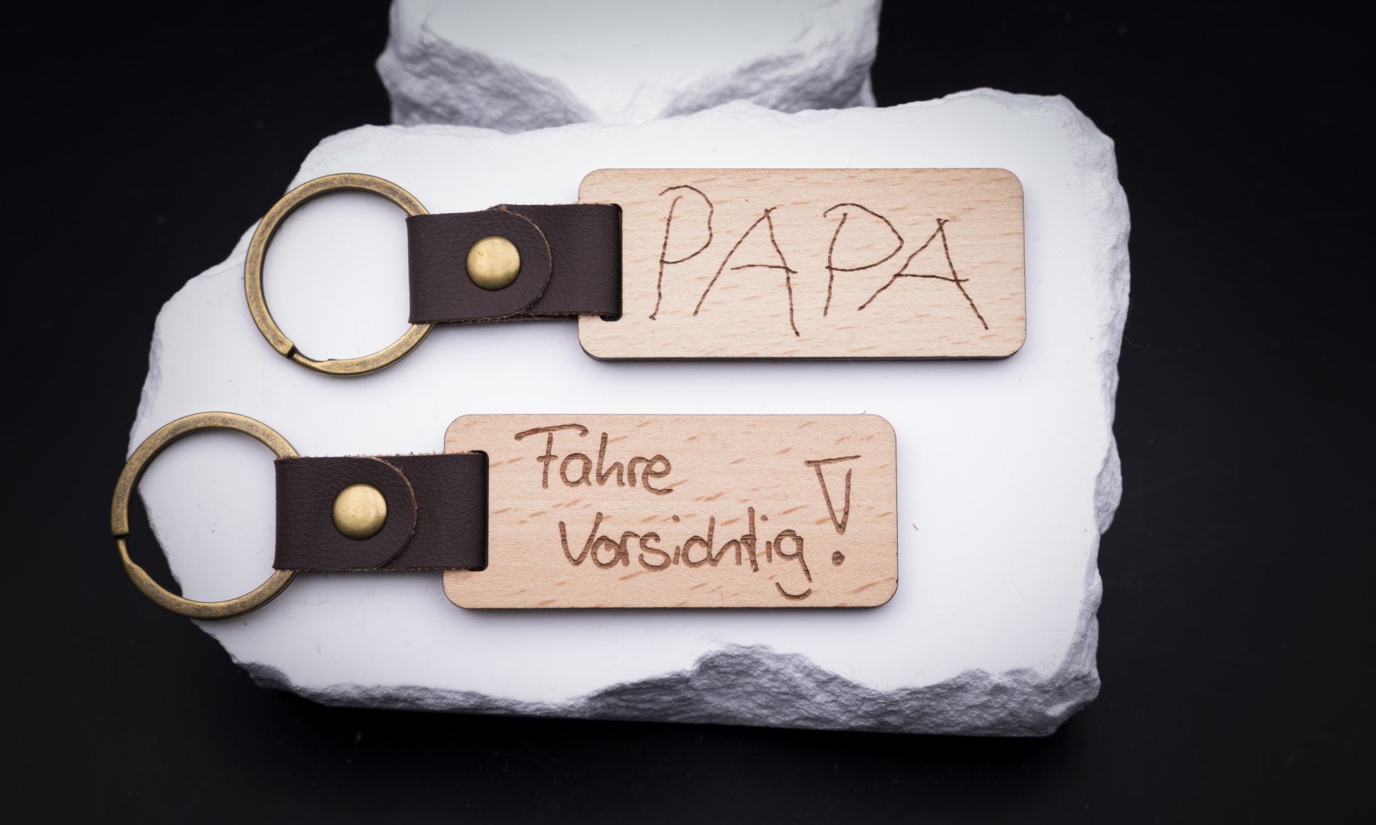 Zwei gravierte Holzschlüsselanhänger mit Lederriemen und goldenen Ringen, die liebevolle Nachrichten enthalten.